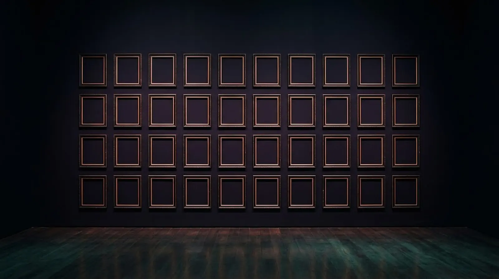 A dark gallery wall of empty frames lit in warm copper